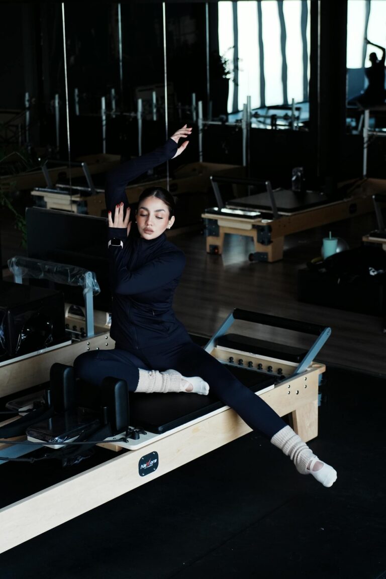 Woman performing stretching exercise on a pilates reformer machine in a gym setting.